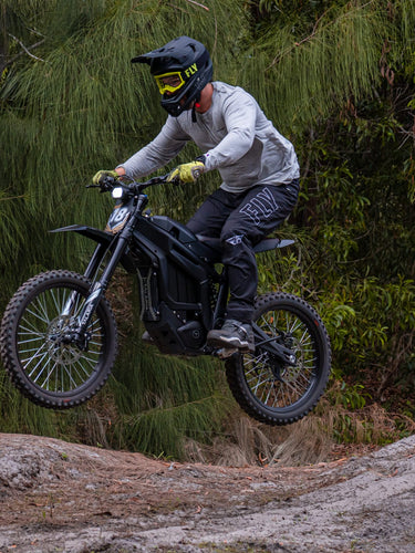 Rider jumping over dirt mound on Talaria Sting R MX4 electric dirt bike with forest background