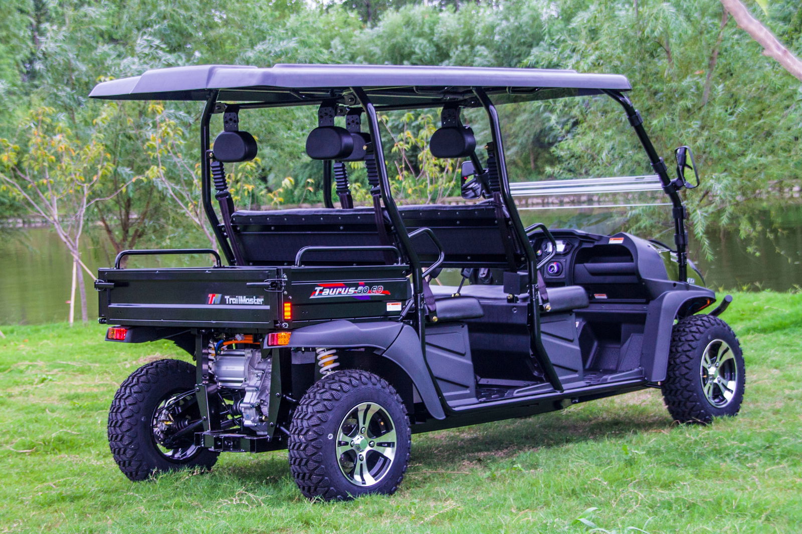 TrailMaster Taurus 80ED 4-Seat Electric Golf Cart with dump bed and aluminum alloy wheels, parked on grass with trees in the background.