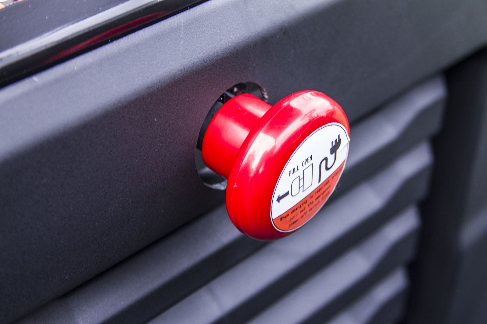 Close-up of a red manual override pull button on an electric golf cart, featuring a warning label and black background.