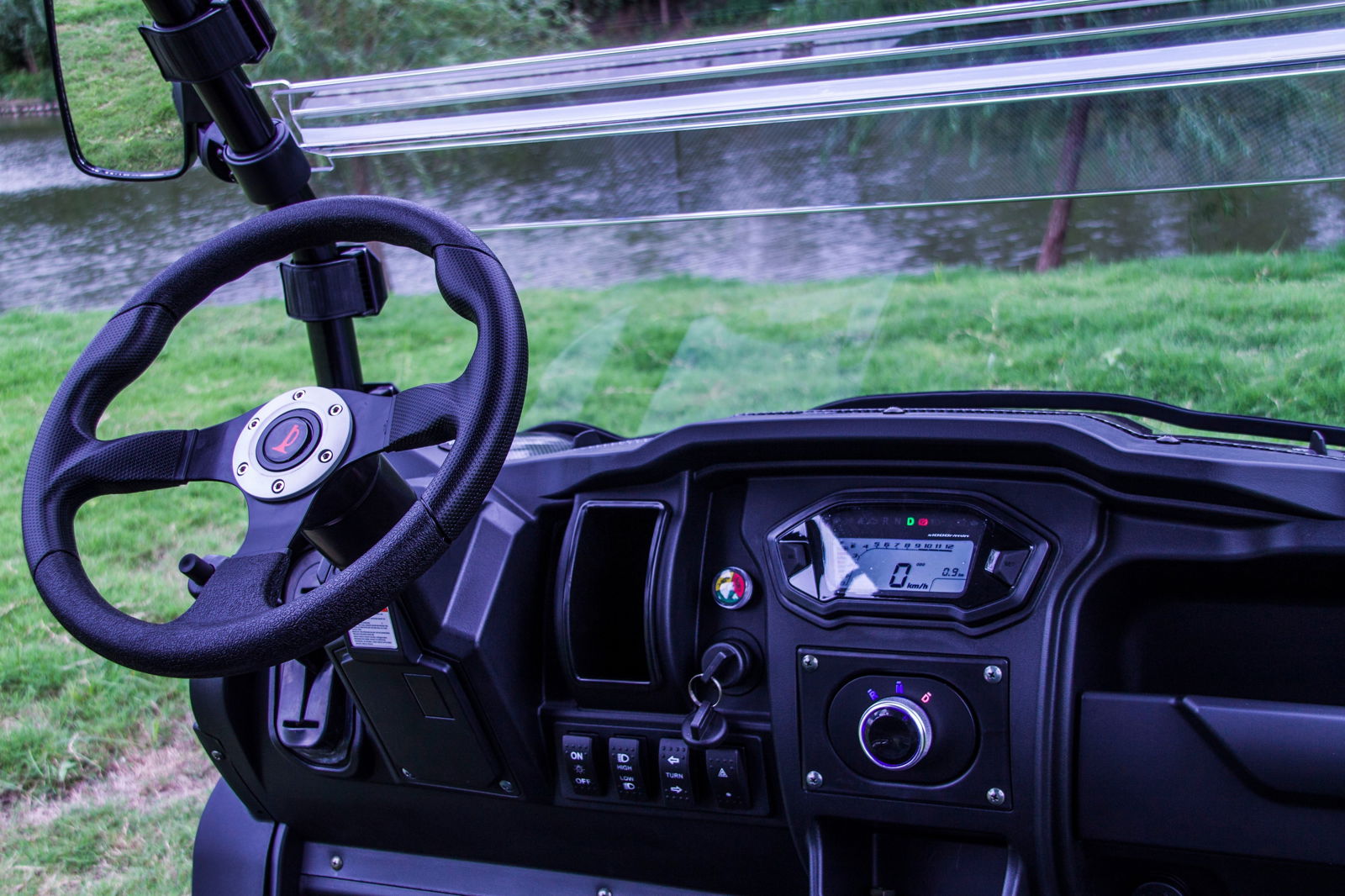 Interior dashboard and steering wheel of TrailMaster Taurus 80ED-U Electric Golf Cart overlooking scenic water and grass backdrop.